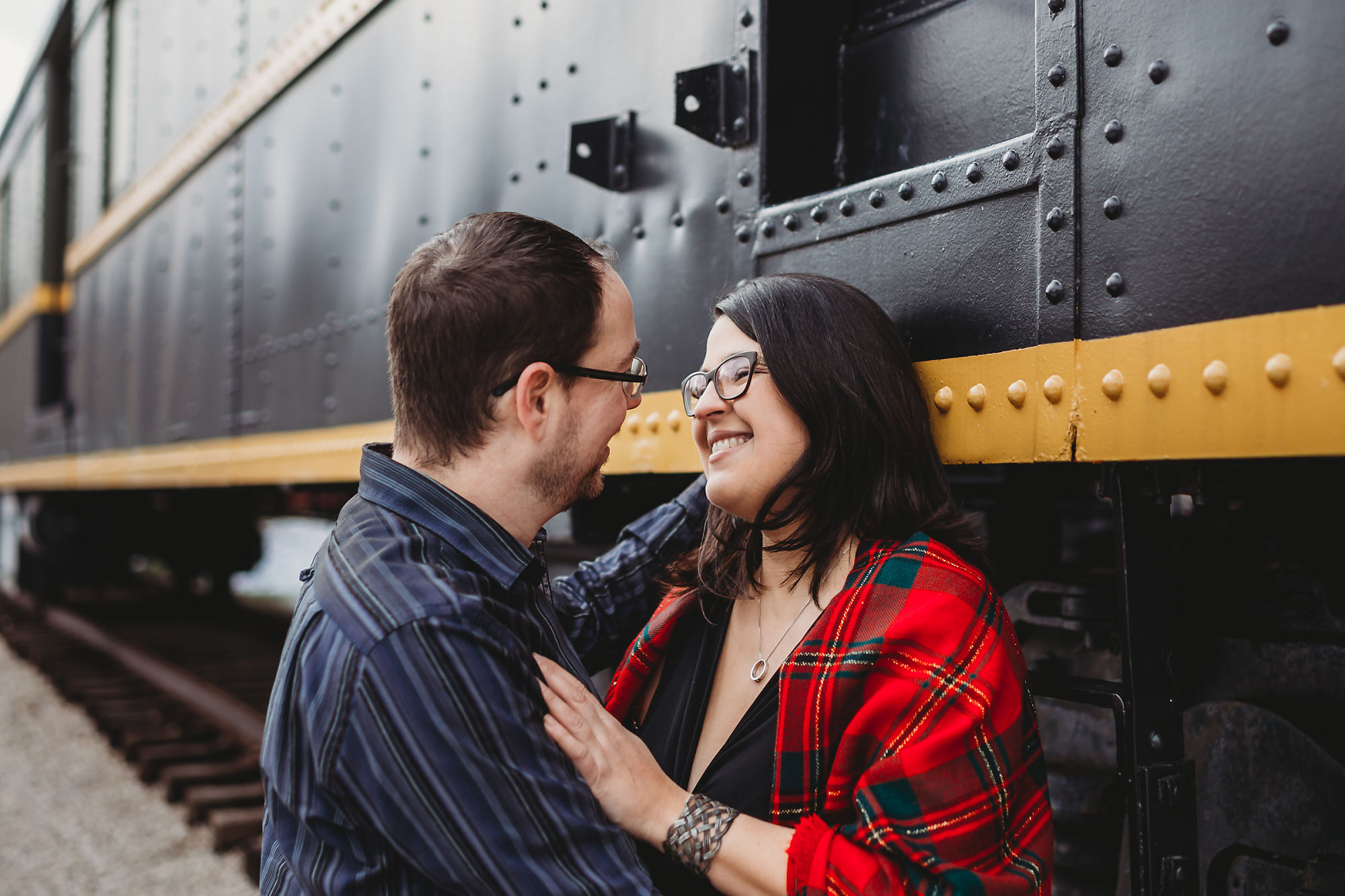 Andy & Erin embrace in front of a museum train at Dundas Conservation Area in Hamilton Ontario during their maternity photoshoot with Dundas Maternity Photographer Jennifer Blaak.